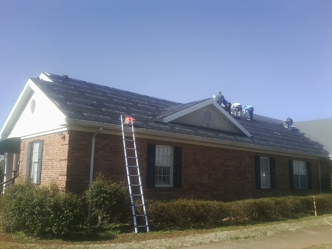 Crew tearing shingles off a brick ranch roof with a ladder set — Emergency Roof Repair work by our crew in Abbeville